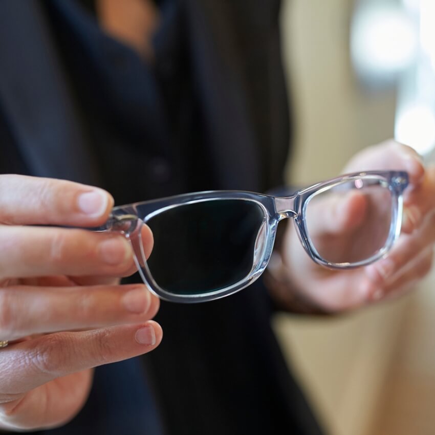 Hands holding a pair of translucent gray eyeglasses with clear lenses.