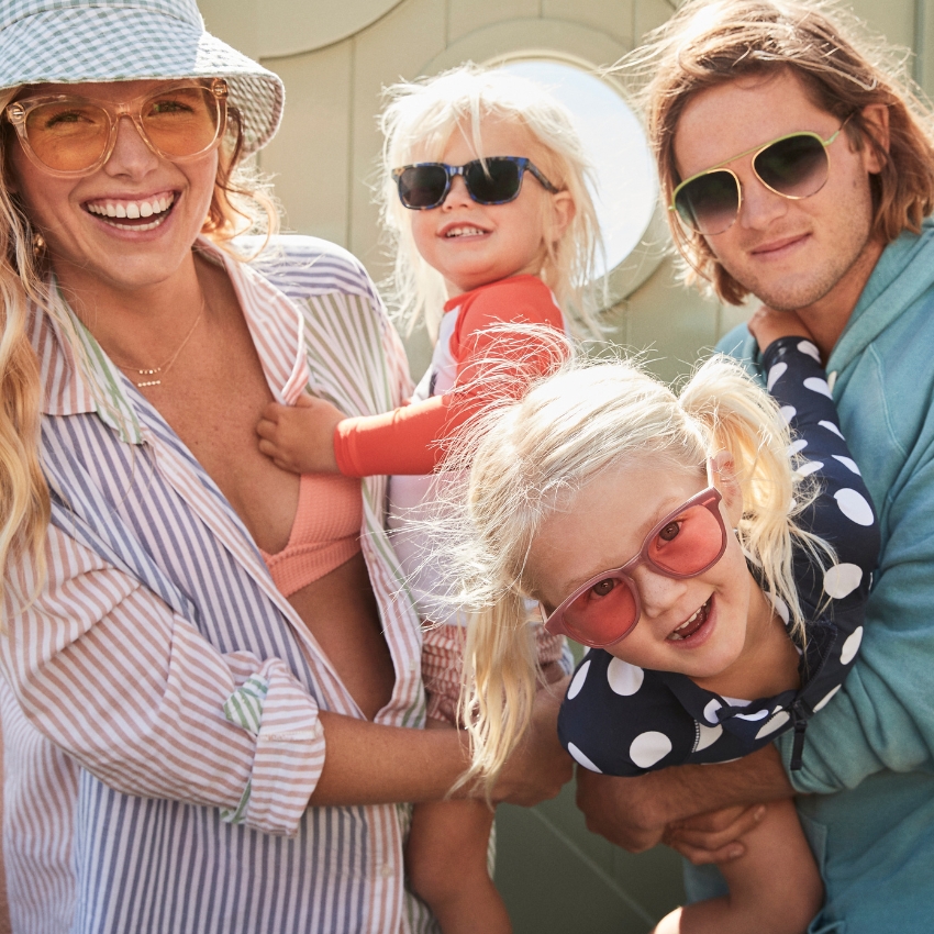 Family wearing colorful sunglasses and casual summer outfits, smiling and posing together.