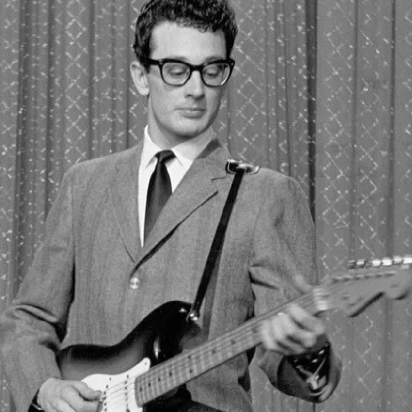 Man playing a vintage electric guitar while wearing a suit and tie.