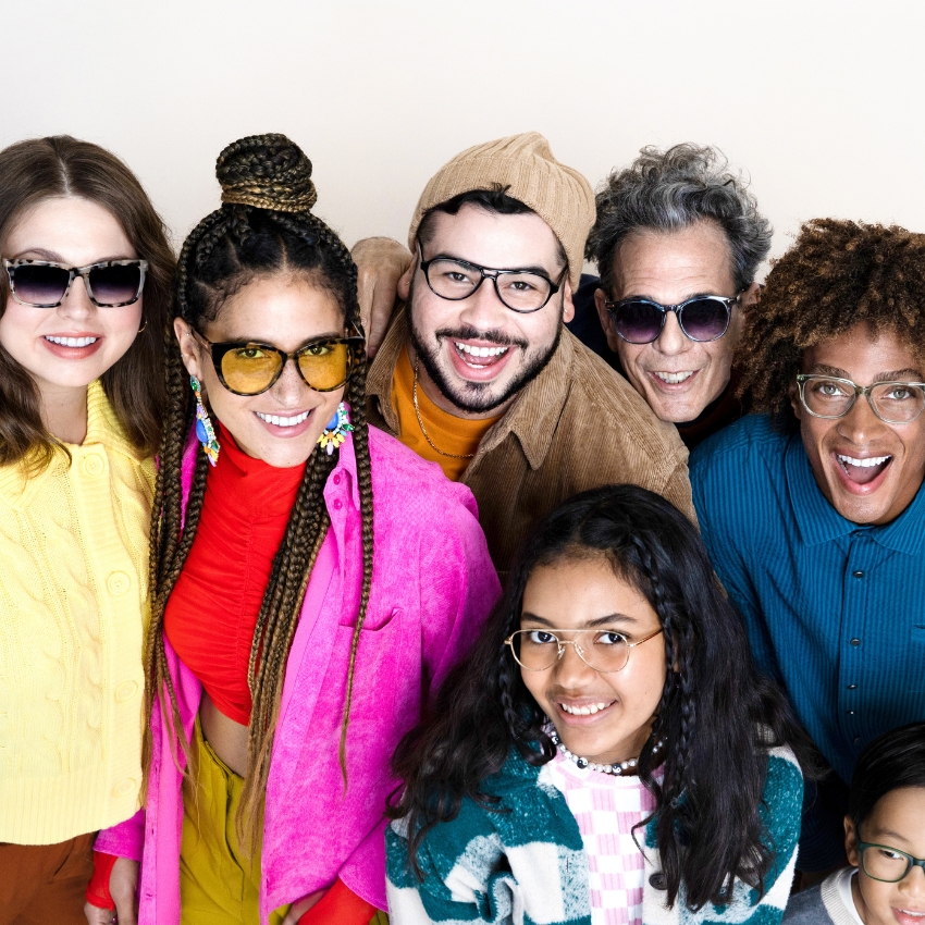 Group of people wearing various styles of eyeglasses, smiling and showing different frames and designs.