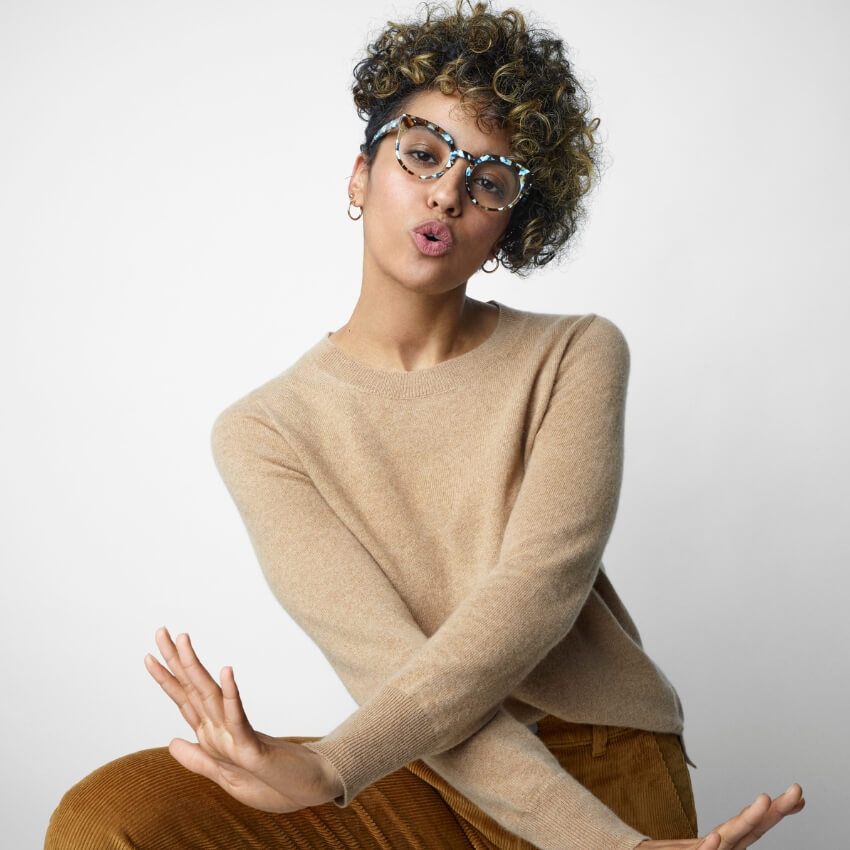 Person wearing blue patterned glasses, camel-colored sweater, and brown corduroy pants.