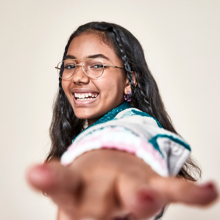 Girl wearing glasses and smiling broadly, reaching out toward the camera.