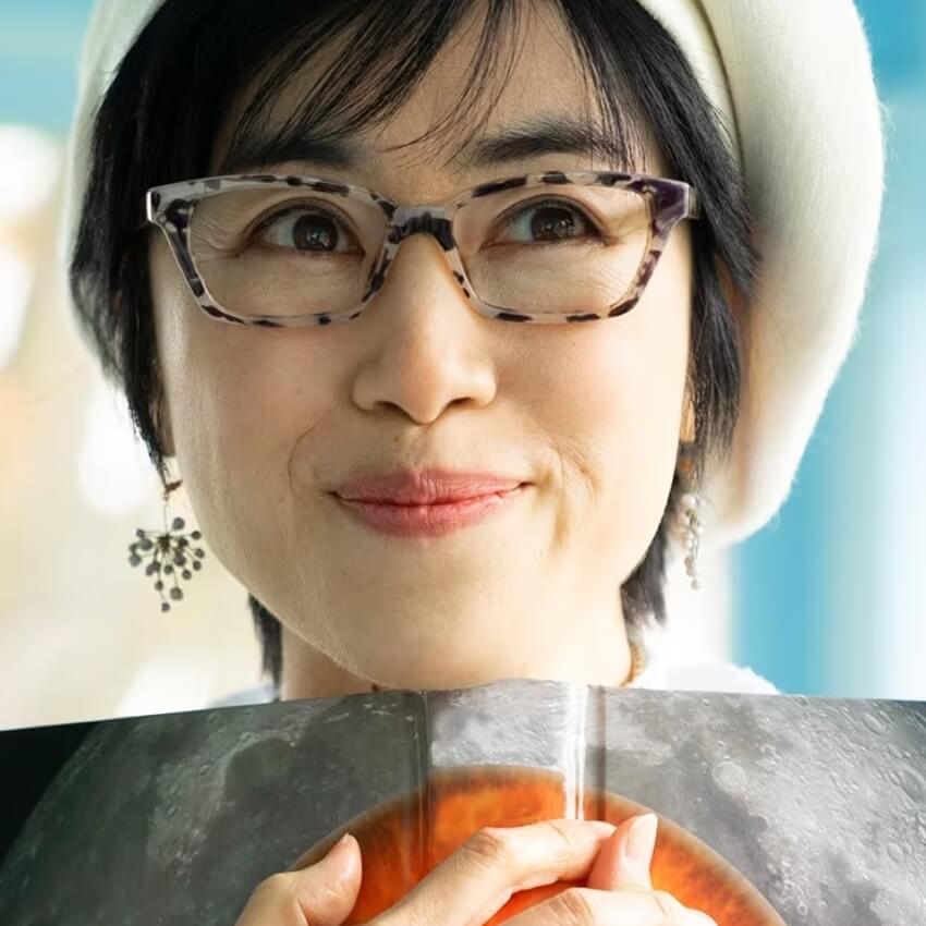 Woman wearing tortoiseshell eyeglasses, white beret, holding a book with a moon and eclipse image.