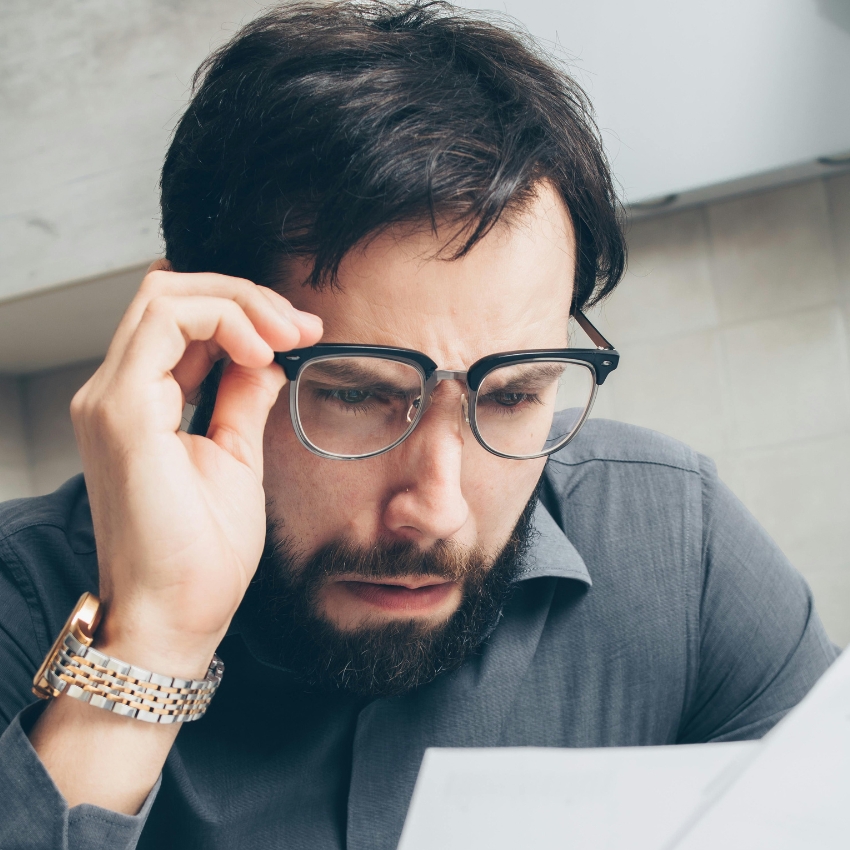 Man in glasses holding a paper, looking concerned and confused.