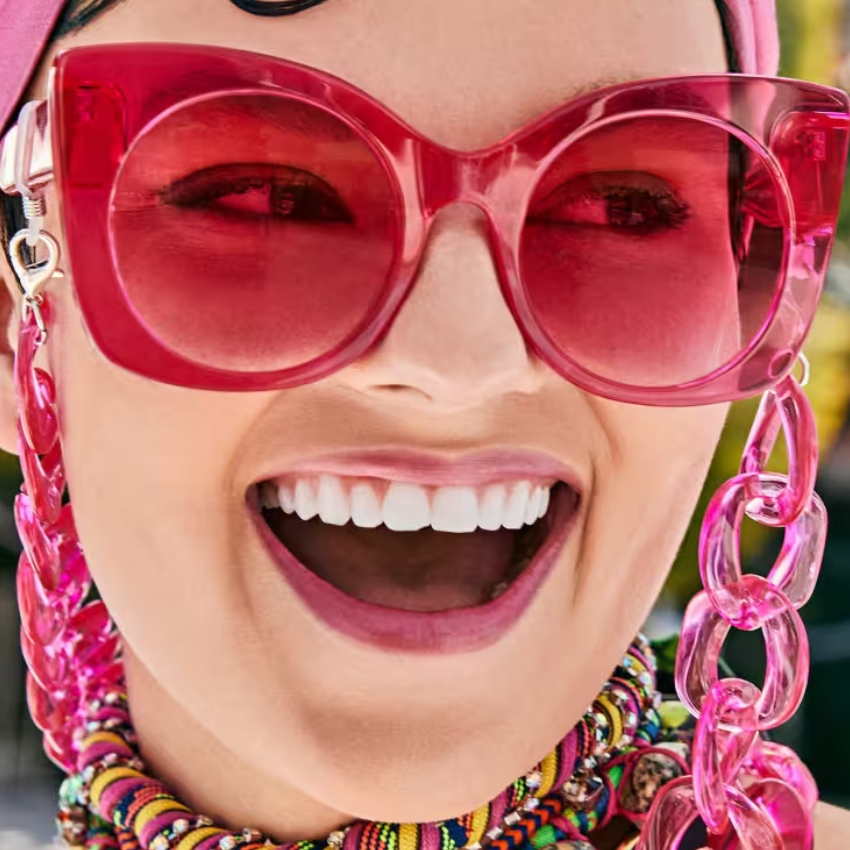 Woman wearing oversized red sunglasses with pink chain and multicolored beaded necklace.