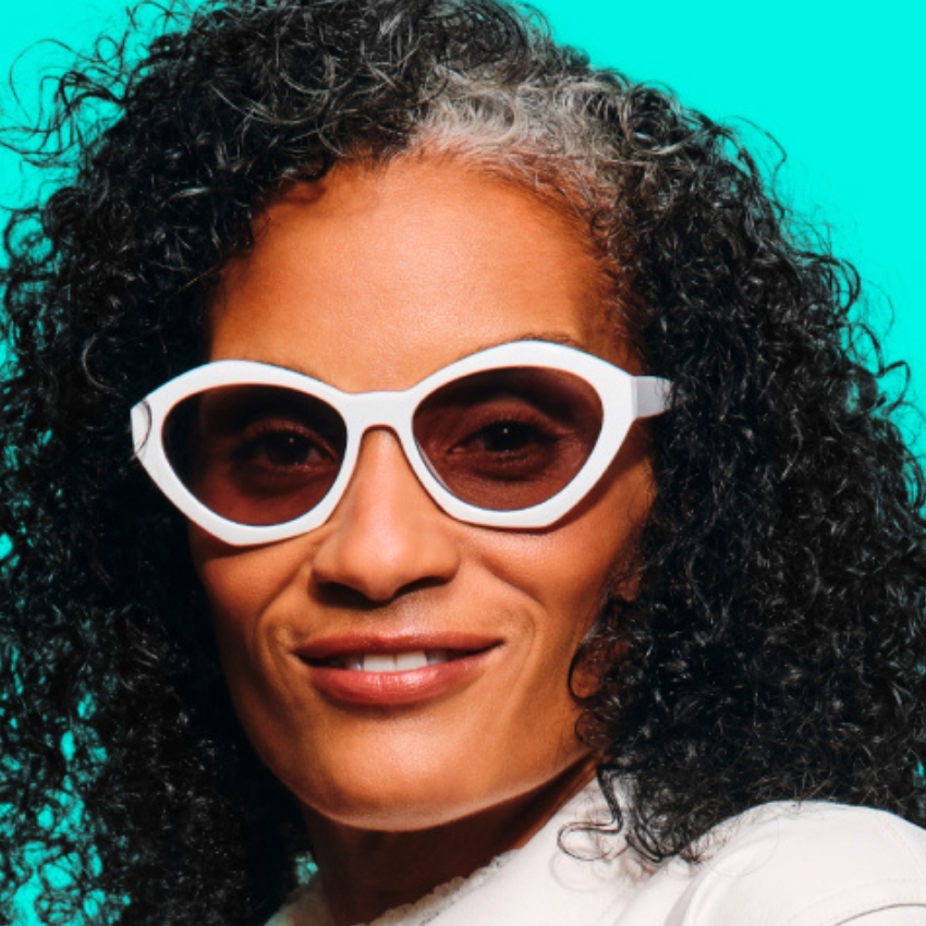 Woman wearing white-framed, oval sunglasses with dark lenses.