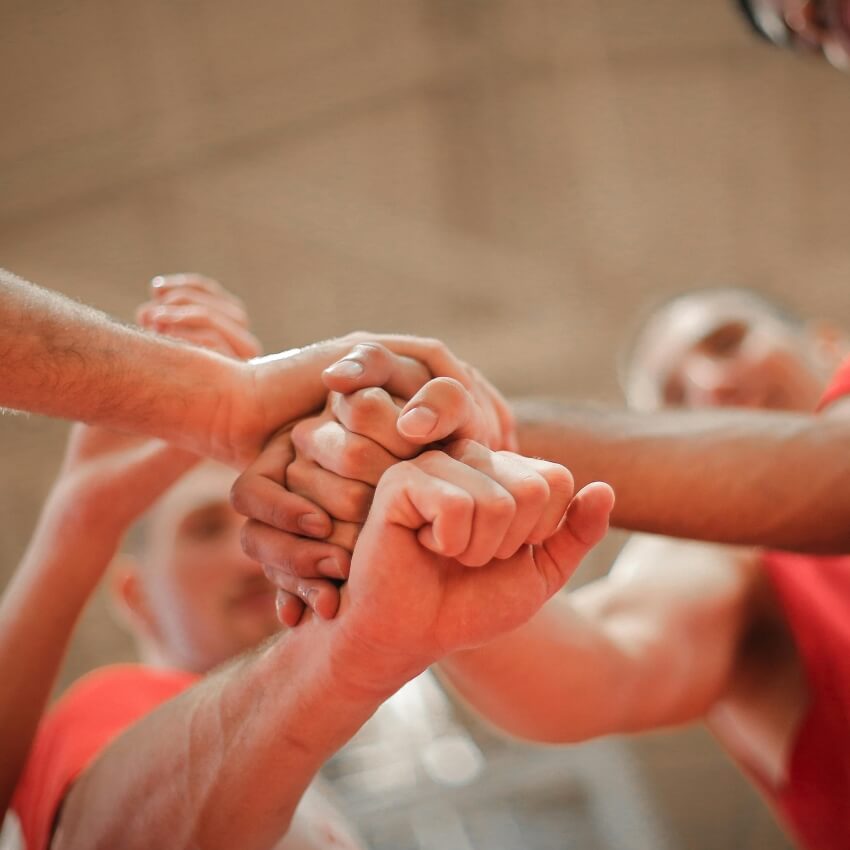 Hands of multiple individuals joined together in a team huddle.