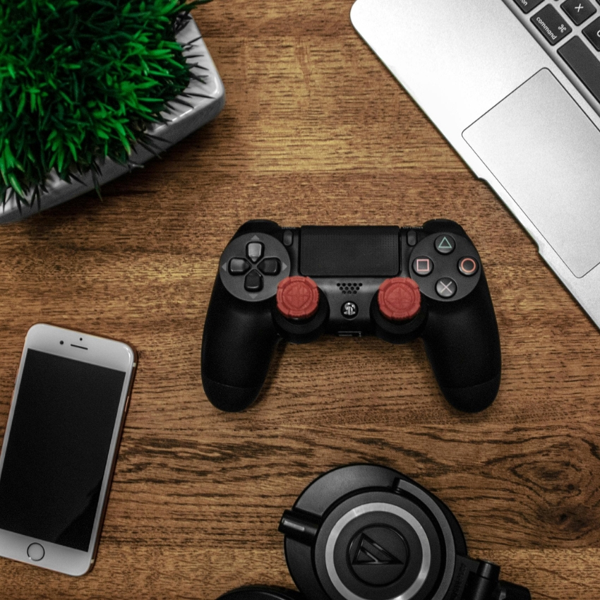 A black gaming controller with red thumb grips on a wooden table.