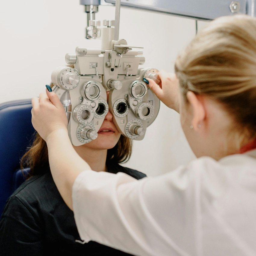 Optometrist adjusting a phoropter on a patient's face during an eye examination.