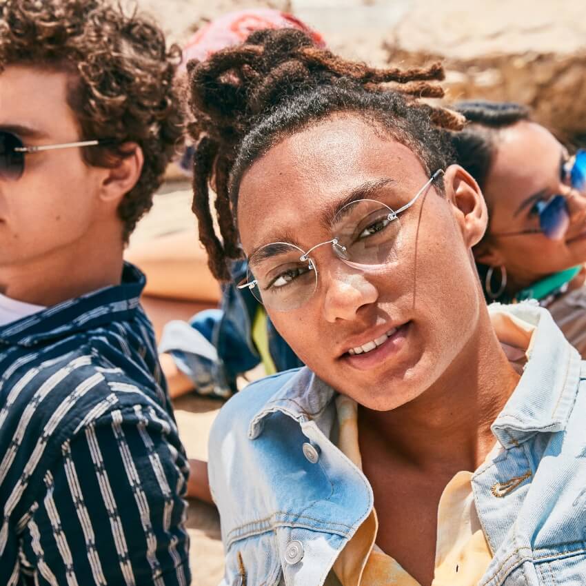 Person wearing clear-rimmed glasses with circular lenses and a light denim jacket.