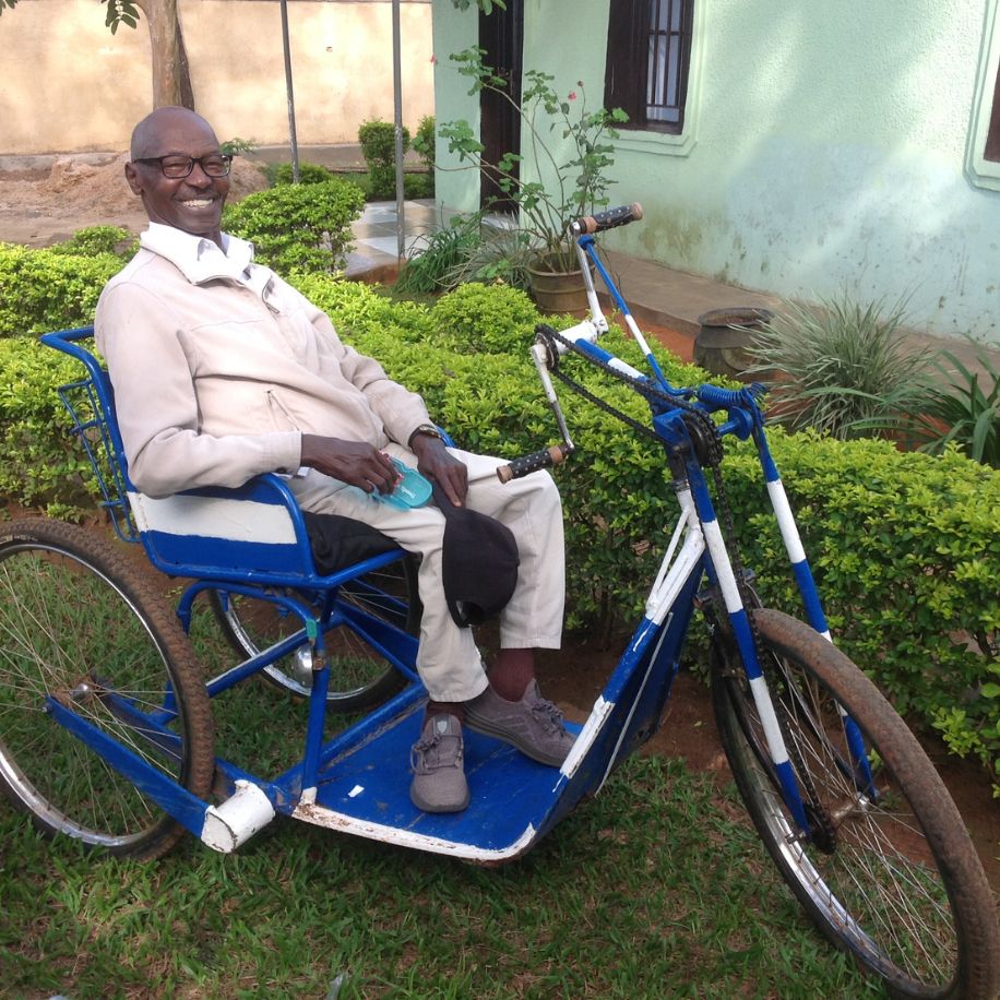 Man smiling while seated on a blue and white three-wheeled mobility tricycle for adults.