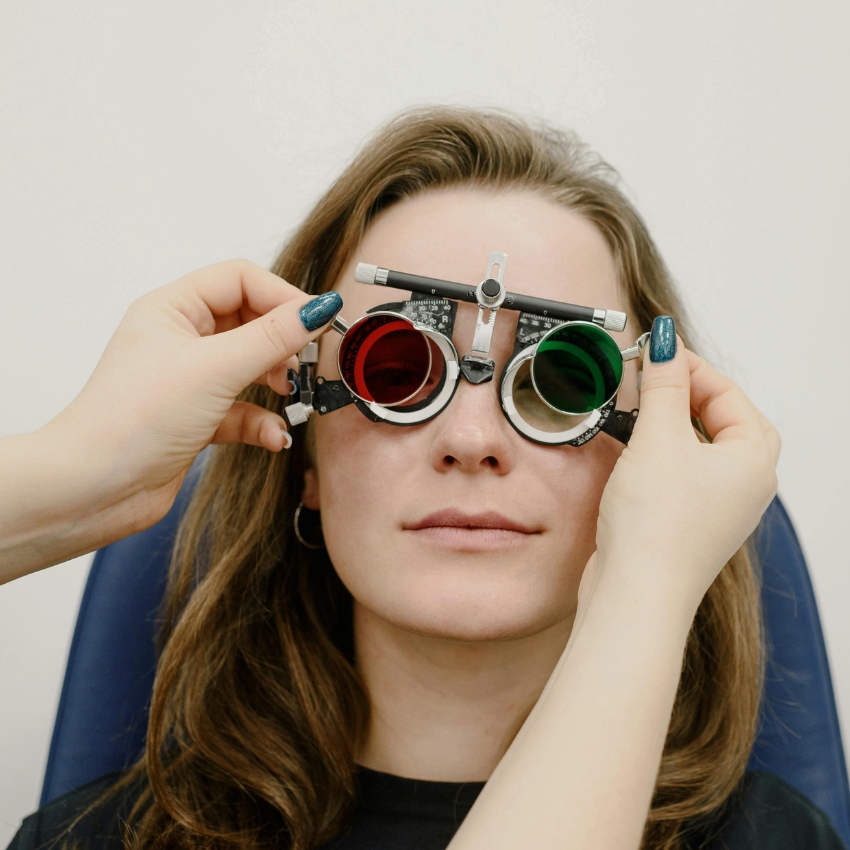 Trial frames with red and green lenses being adjusted on a woman's face during an eye exam.