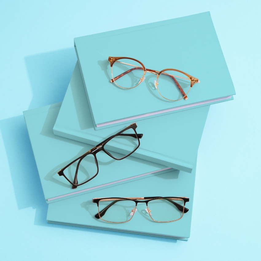 Three pairs of eyeglasses on stacked blue books with pastel background.