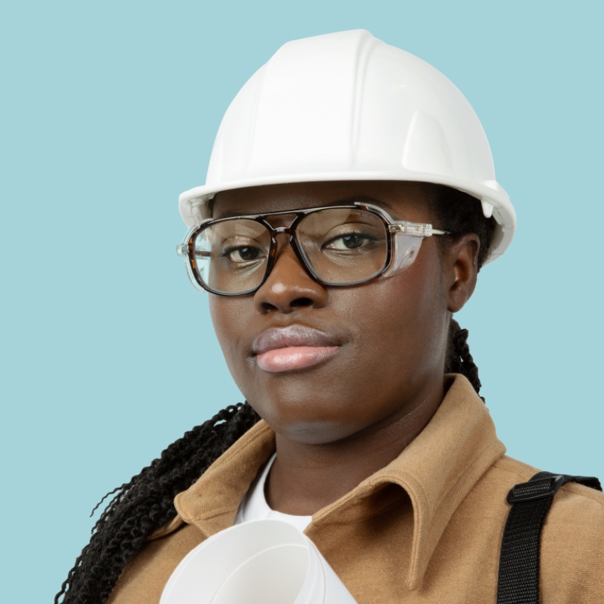 Person wearing a white hard hat and clear safety glasses, holding rolled architectural plans.