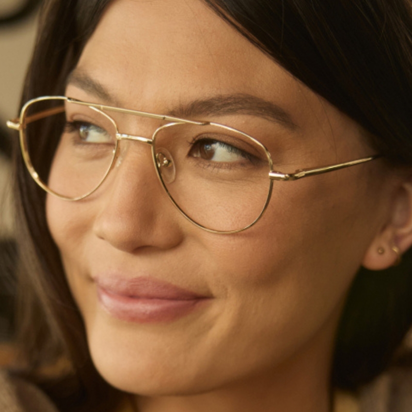 Gold-rimmed eyeglasses with thin, delicate frames and clear lenses worn by a person looking to the side.