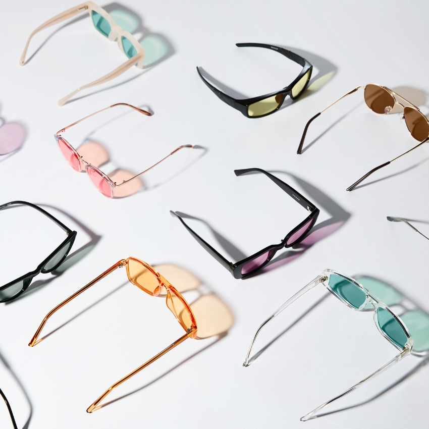 Colorful collection of sunglasses with various frame shapes and tinted lenses displayed on a white surface.