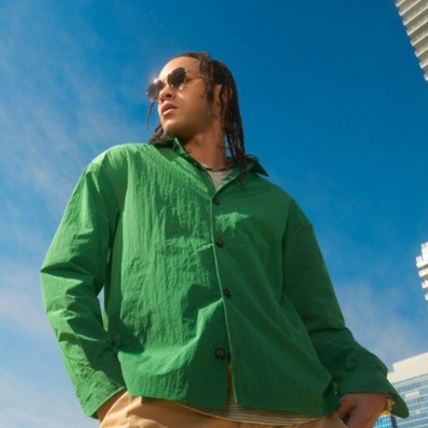 Person wearing a bright green button-up shirt and sunglasses against a clear blue sky.