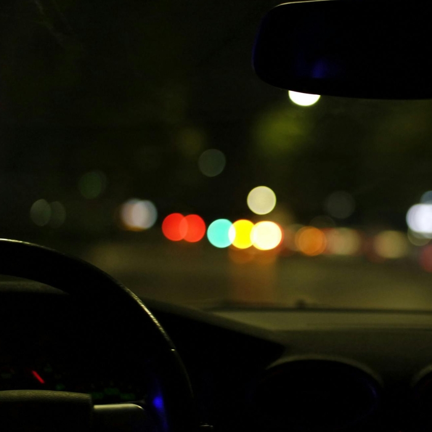 Night view from inside a car with a blurred cityscape and traffic lights ahead.