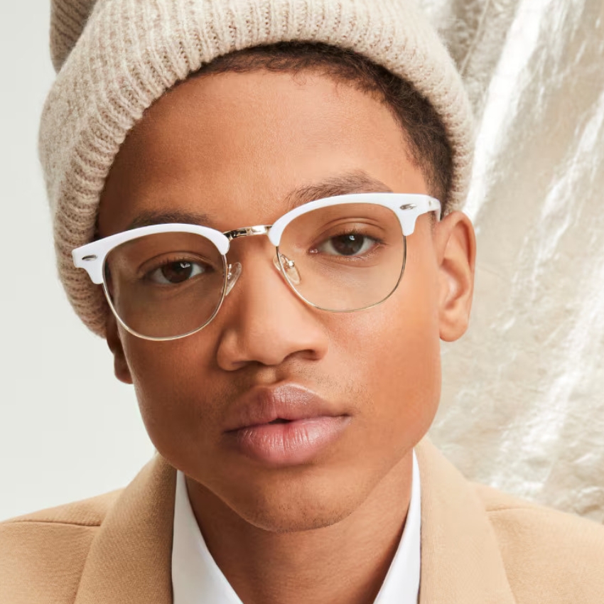 Man wearing beige knitted beanie, light tan blazer, and white-rimmed eyeglasses with metal bridge and hinges.