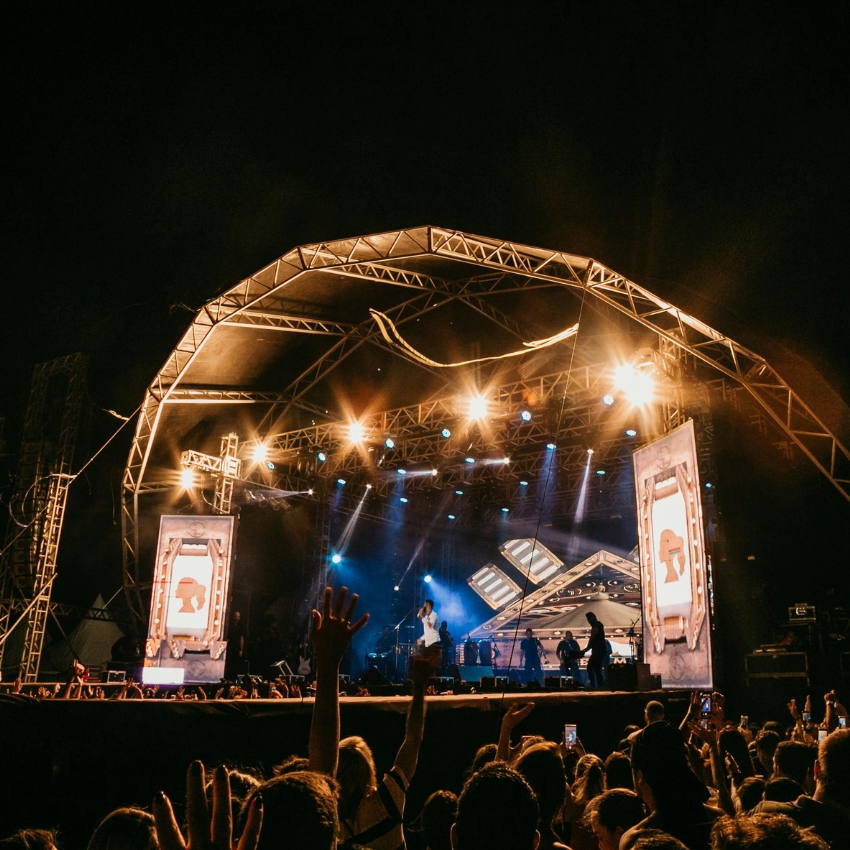 Large concert stage with bright lights, two large screens on each side displaying abstract art.