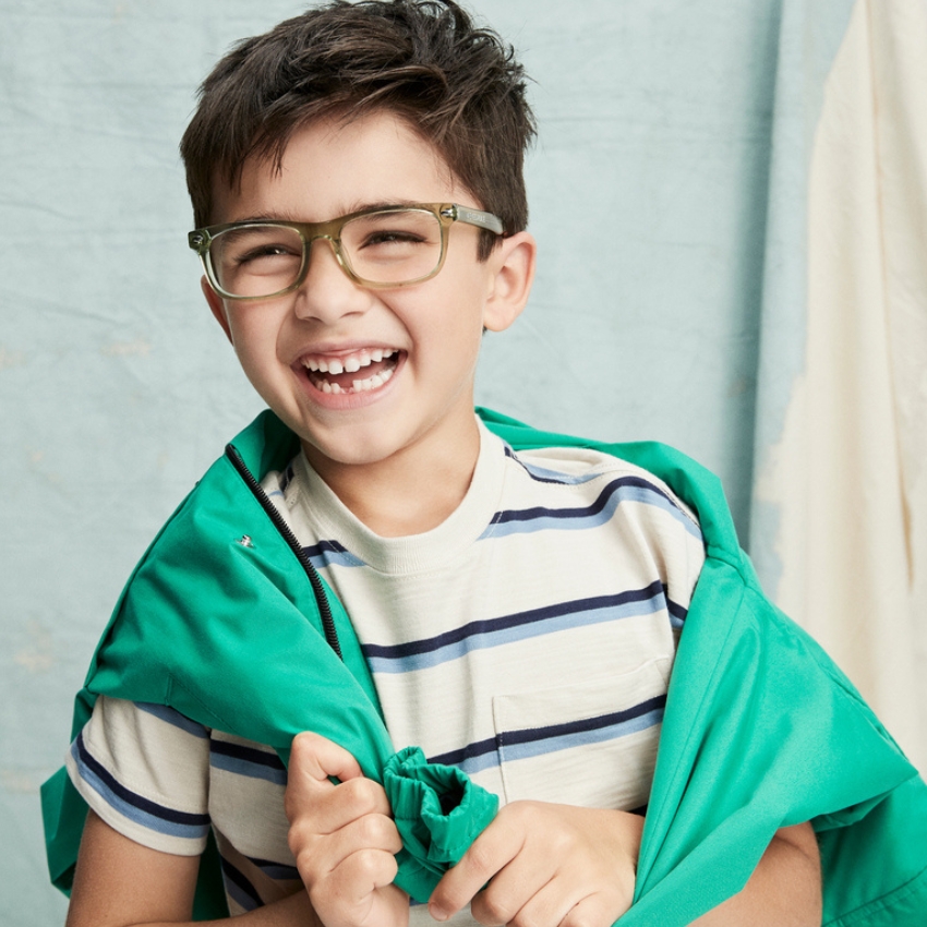 Boy wearing green glasses with a striped shirt, smiling while holding a green jacket.