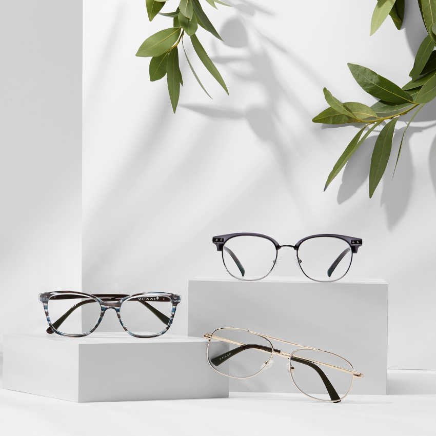 Three pairs of eyeglasses displayed on white blocks; one with black frames, one with tortoiseshell frames, and one with gold wire frames.