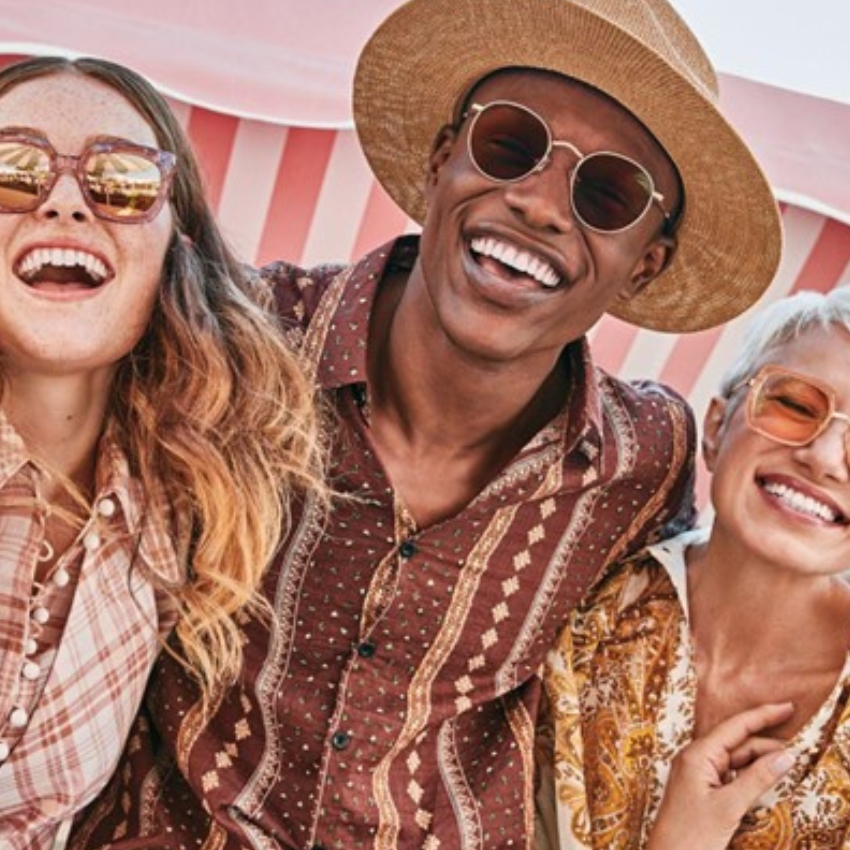 Three people wearing stylish sunglasses and patterned shirts, smiling joyfully.