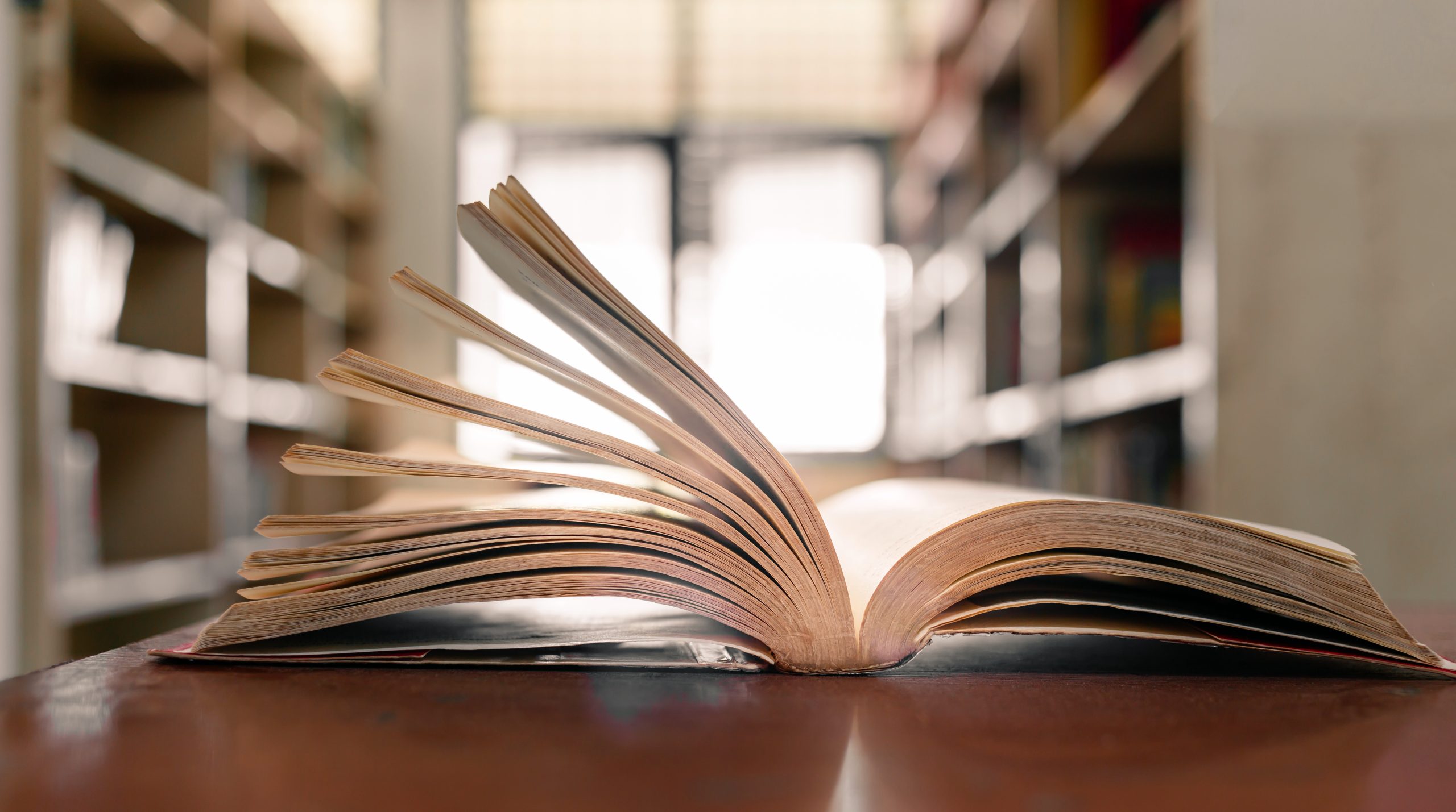 Open book with pages fanned out, lying on a wooden surface.