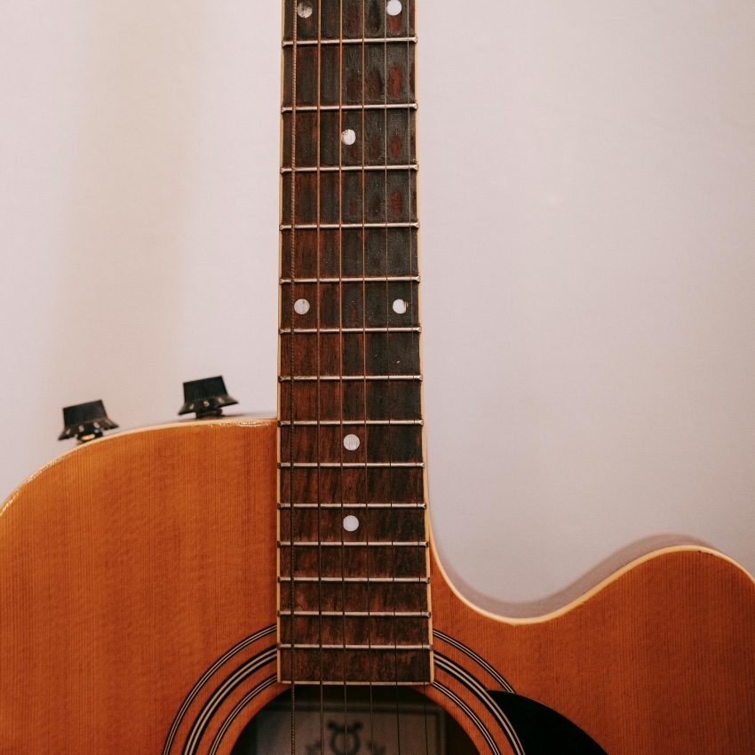 Brown acoustic guitar neck and body, showing frets, strings, and soundhole with rosette.