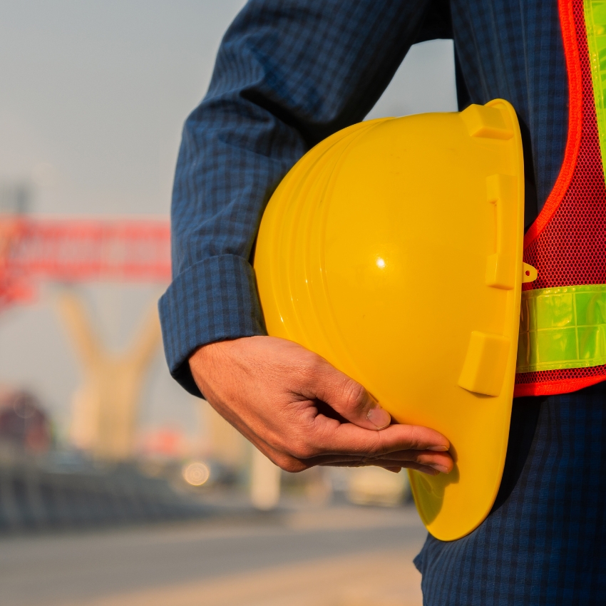 Person holding a yellow hard hat, dressed in a blue shirt and an orange safety vest.