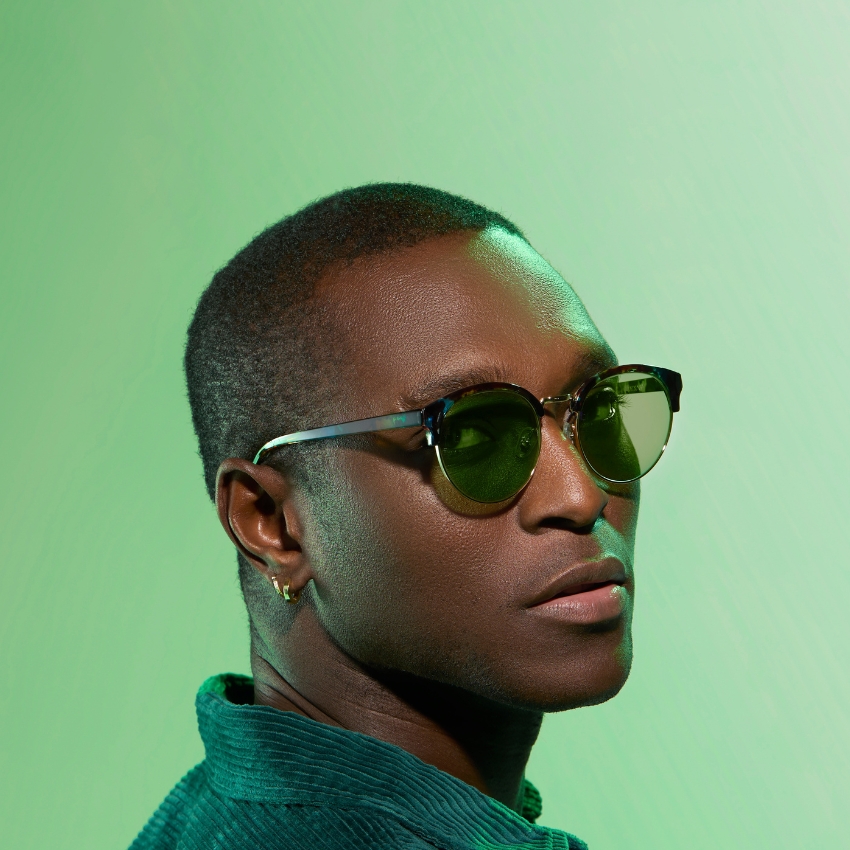 Man wearing stylish sunglasses with green lenses and a green collared shirt, against a green background.