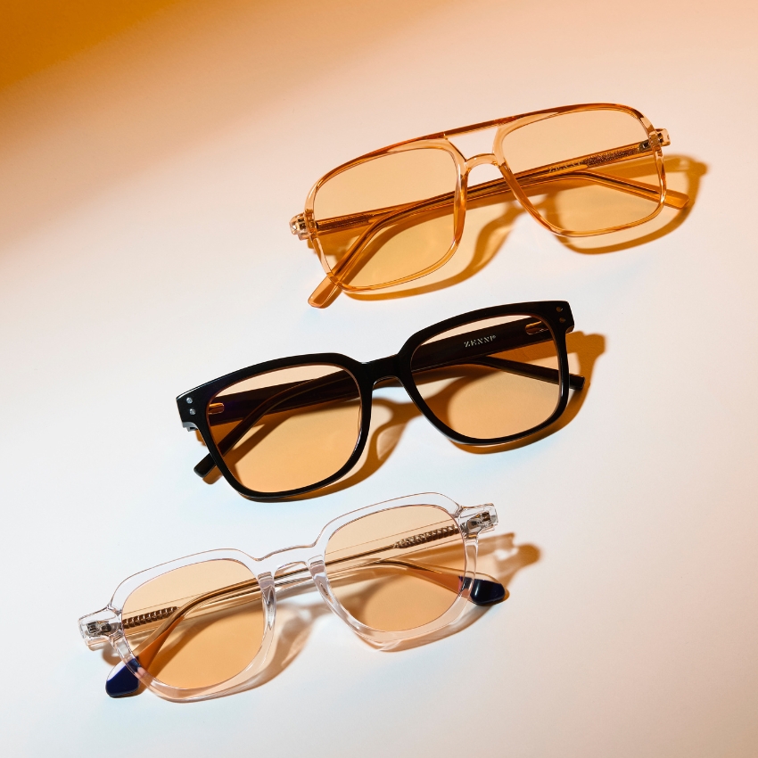 Three pairs of eyeglasses with colored lenses: one gold-framed, one black-framed, and one clear-framed.