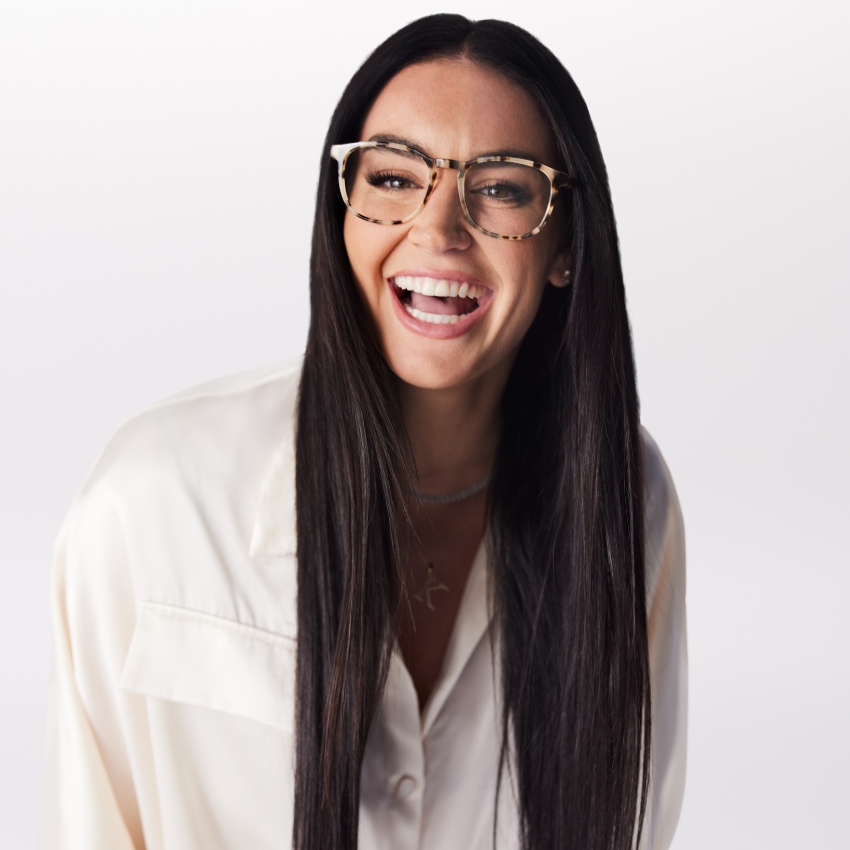 Woman wearing tortoiseshell eyeglasses, smiling, and dressed in a white button-up shirt.