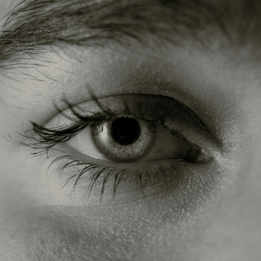 Close-up of a human eye with detailed lashes and skin texture in black and white.