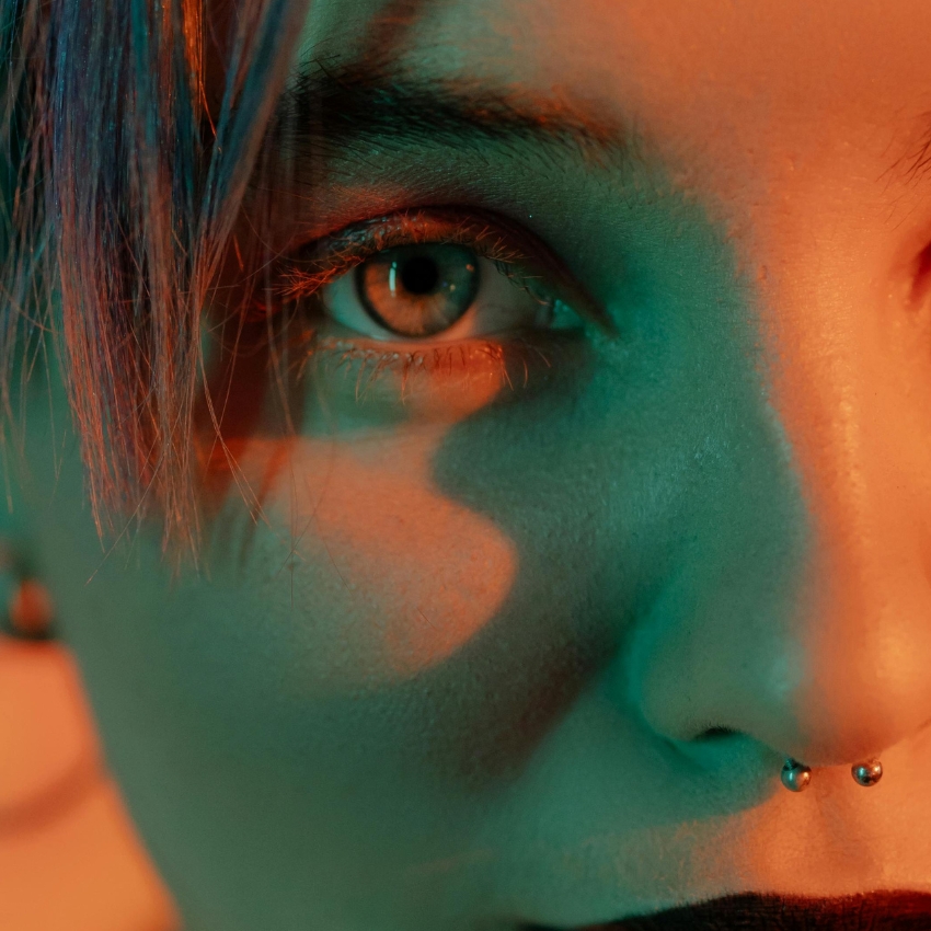 Close-up of a face with colorful lighting, highlighting a double nose piercing and light makeup.