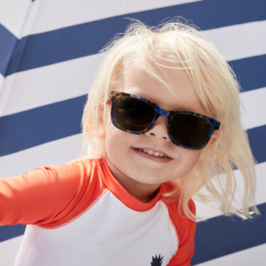 Child wearing sunglasses and an orange and white rash guard.