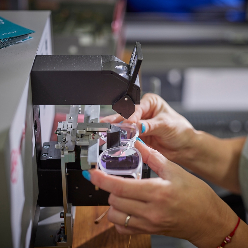 Hands positioning eyeglasses into a lens edging machine for shaping and fitting lenses.