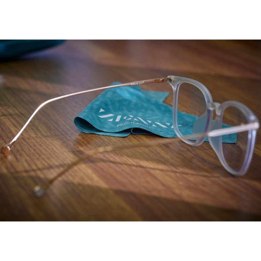 Translucent eyeglasses with gold temples near a teal cloth with white "ZENNI" text.