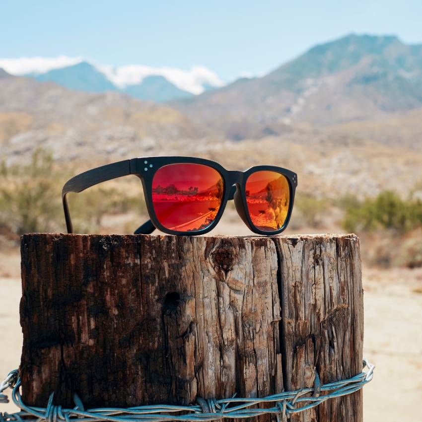 Black sunglasses with red reflective lenses placed on a weathered wooden post.