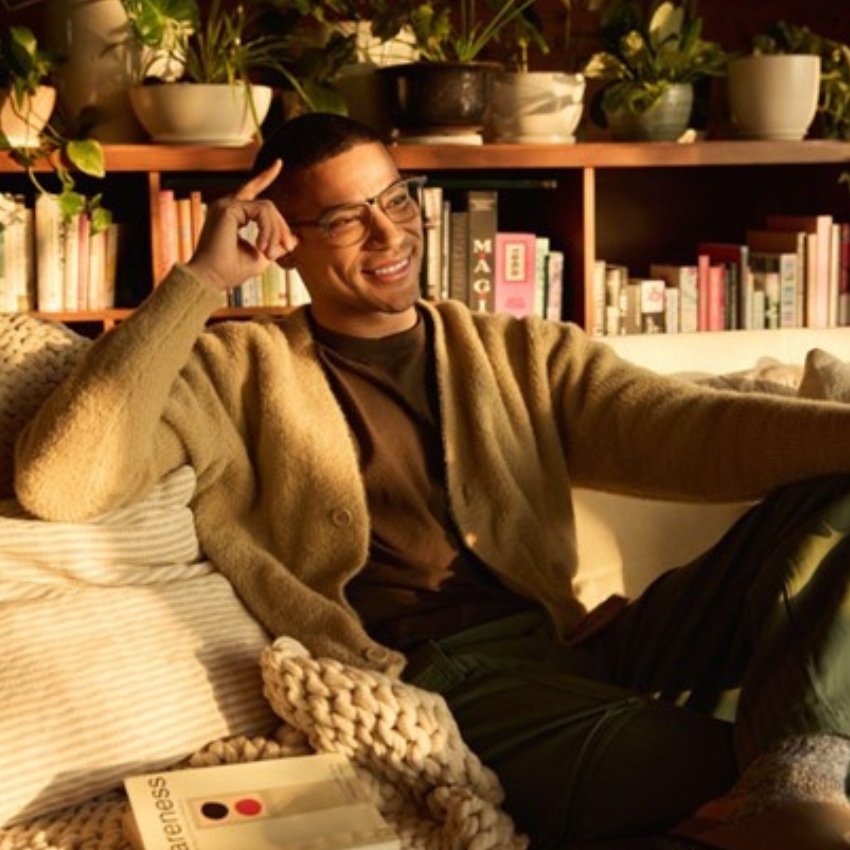 Smiling person wearing glasses and a tan cardigan; book titled "awareness" on a knitted blanket.