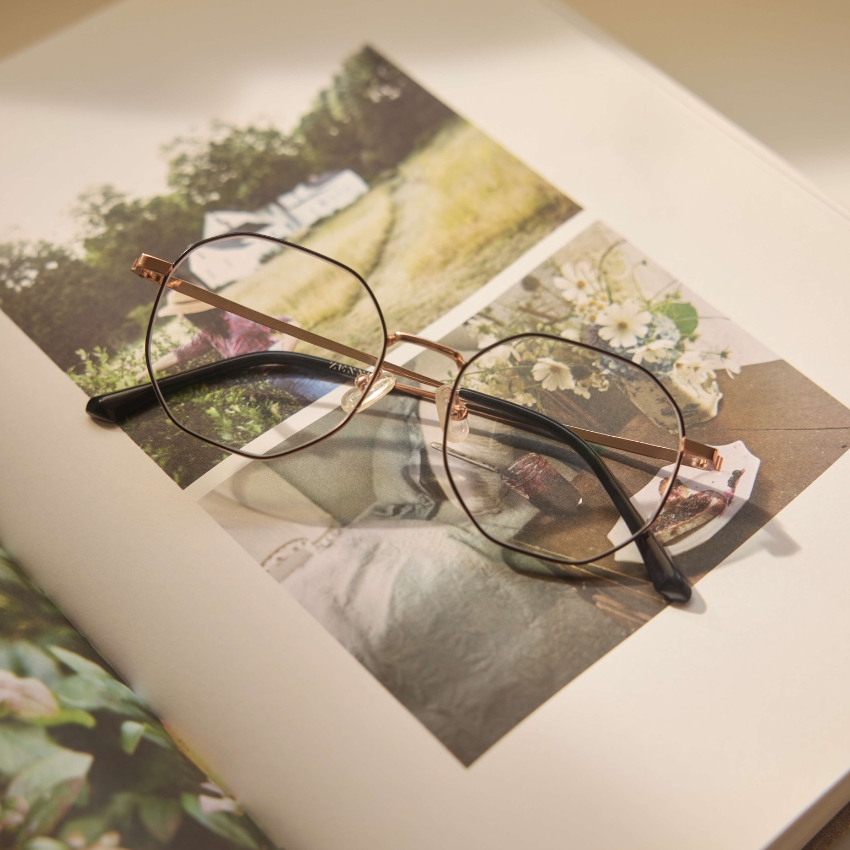 Thin metal-framed glasses resting on an open book displaying photos of nature and a flower arrangement.