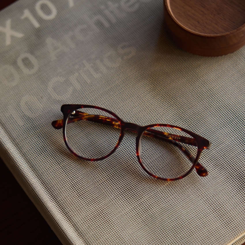 Tortoiseshell round eyeglasses resting on a gray mesh surface, partially covering a book.