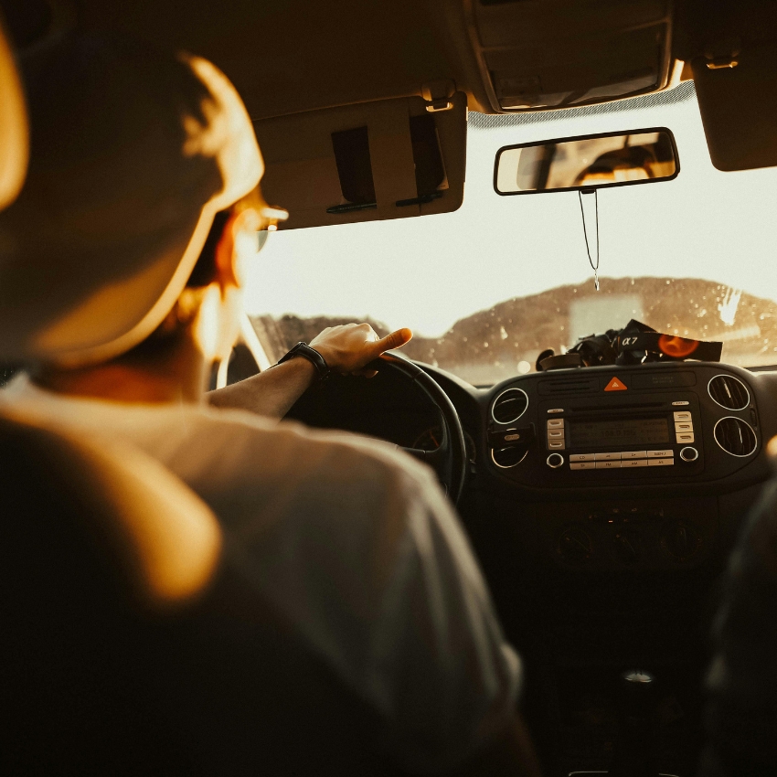 Person driving a car, dashboard with controls and a hanging object from the rearview mirror.