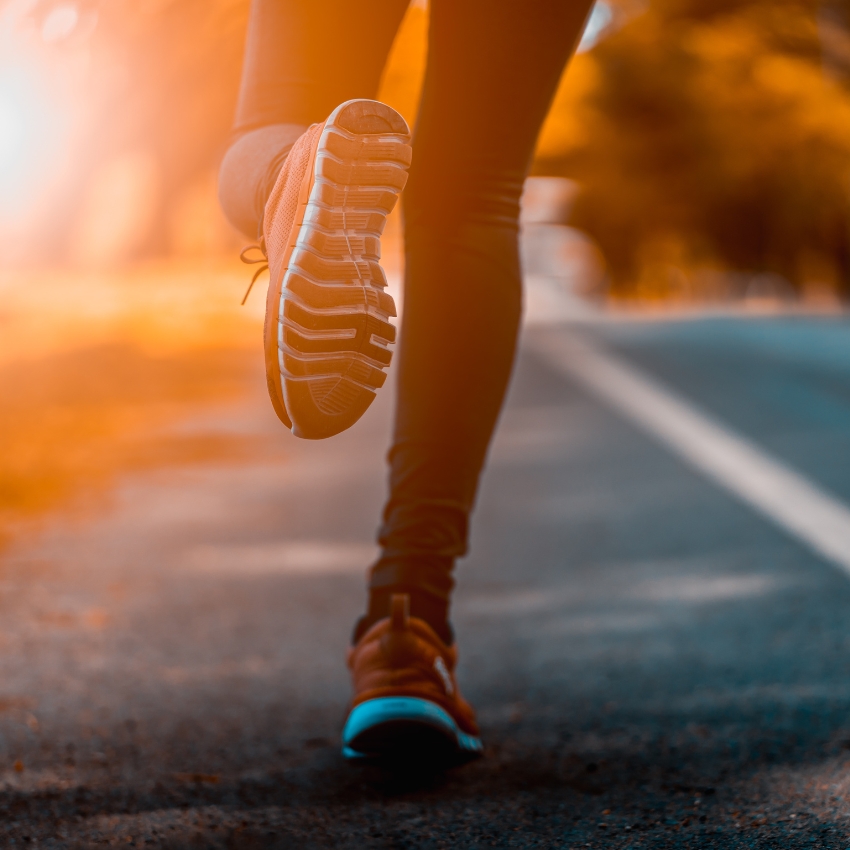 Runner's foot in orange athletic shoe hitting the pavement during a run at sunrise.