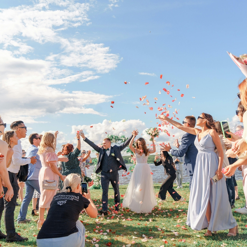 A bride and groom celebrating outdoors as guests throw rose petals. Bride in white, groom in dark suit.