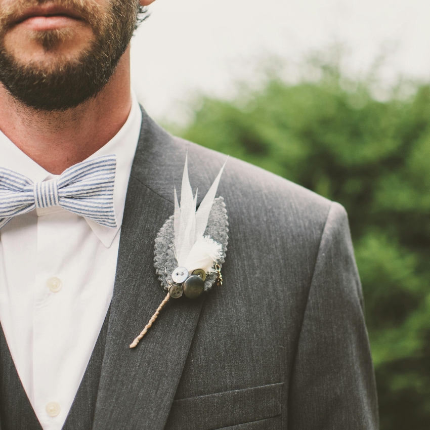 Gray suit with a striped bow tie and boutonniere featuring buttons, feathers, and felt elements.