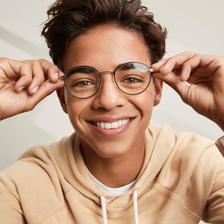 Smiling person wearing round, thin-framed glasses and a beige hoodie.