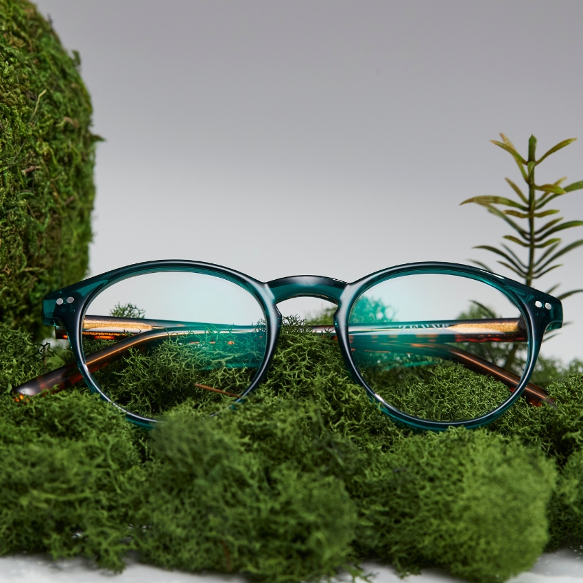 Green eyeglasses with round lenses placed on a bed of green moss.