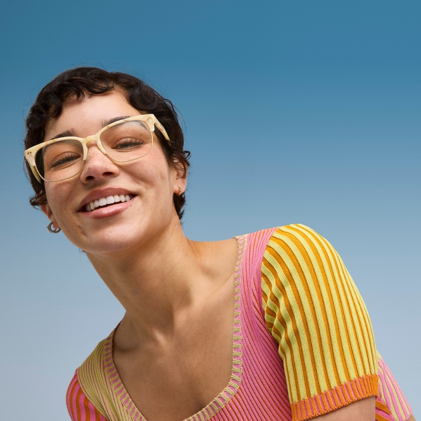 Person wearing tan eyeglasses with a wide smile, dressed in a pink and yellow striped top.