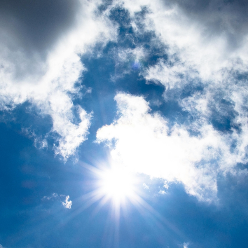 Bright sun shining through scattered clouds in a clear blue sky.